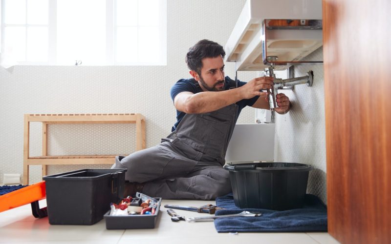 Male Plumber Working To Fix Leaking Sink In Home Bathroom